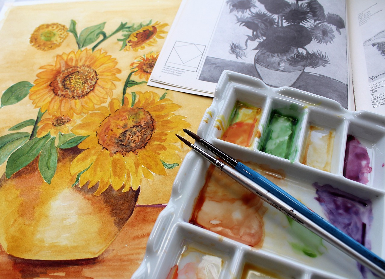 Watercolor painting of sunflowers in a yellow vase alongside a paint palette with yellow, orange, and other colors, illustrating the use of yellow in art and its psychological impact.